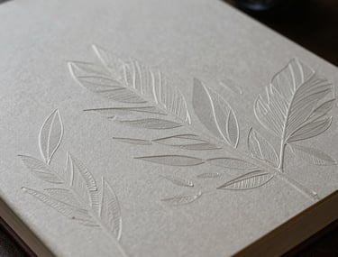An artistic shot of a journal cover with an embossed leaf pattern. The lighting creates subtle highlights on the texture of the paper.
