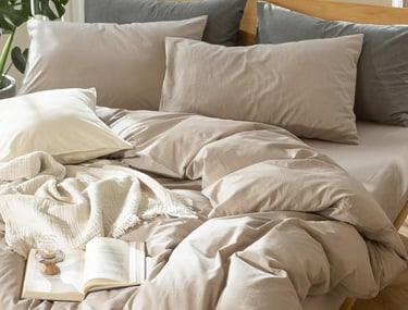 Neutral beige linen bedding set on a wooden frame with grey pillows and a cozy knit throw.