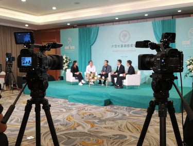 A wide shot of an event venue during a live stream setup. Multiple professional cameras are positioned to capture a panel discussion on a stage decorated with elegant teal fabrics.