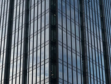 Photography of a modern glass skyscraper reflecting a clear sky. High-contrast composition in Oxford navy and slate gray blue tones. Represents stability and growth.
