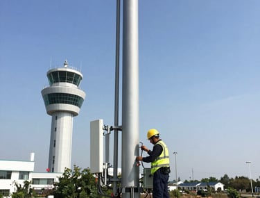 Technician performing maintenance on aircraft electronic systems inside a hangar.