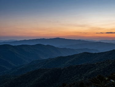 A distant shot of layered mountain ridges under a deep blue and orange sky at sunset, depicting beautiful clean vistas of the Blue Ridge Parkway.