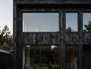 Minimalist photography of a modern home exterior in the Pacific Northwest, featuring dark wood siding and large windows.