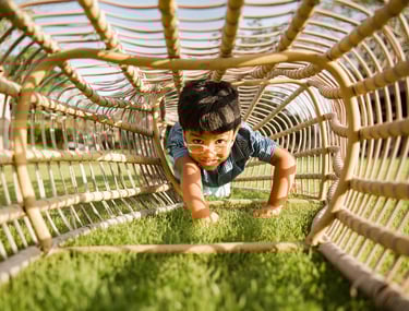 child crawling through rattan tunnel chair on the lawn at rimba by ayana bali during family photography