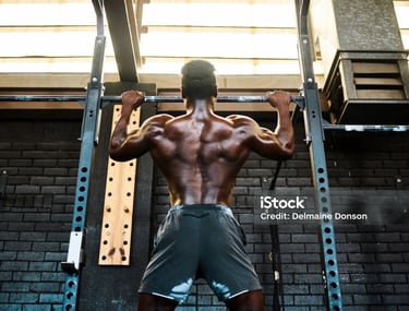 Muscular athlete performing pull-ups on a gym rack to build back muscle strength.