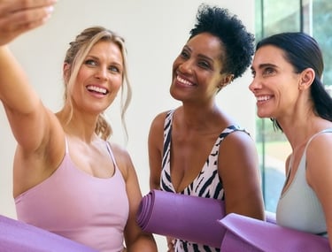 Three diverse women in athletic wear smiling for a selfie after a yoga workout.