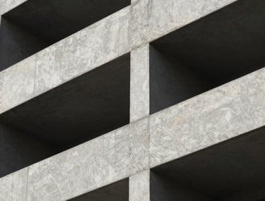 A close-up of high-quality architectural concrete work on a building facade, with sharp shadows creating a play of light. The finish is smooth and premium.