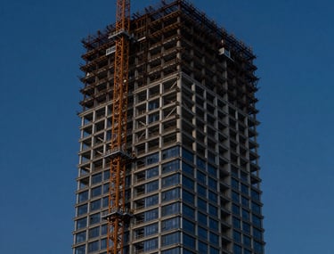 A high-contrast photograph of a modern skyscraper under construction against a deep navy blue twilight sky. The steel framework is precisely captured, highlighting the company's technical expertise.