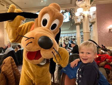 Pluto posing for a photo with a delighted little boy at Disneyland Paris Character Dinner