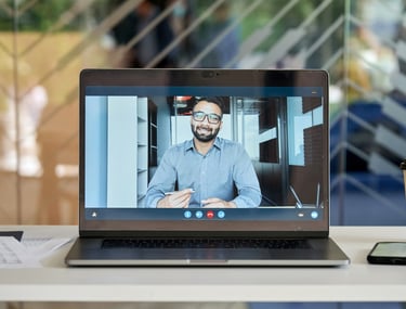 A laptop screen showing a video call with a man in a business shirt holding a pen
