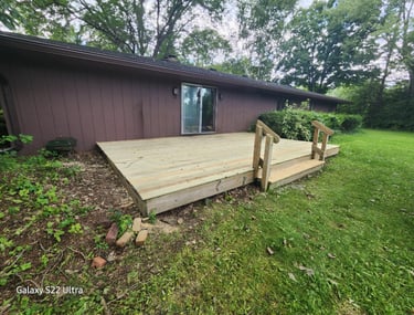 A newly installed wooden backyard deck with steps attached to a brown ranch-style house.
