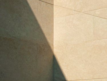 Architectural detail showing the intersection of two smooth sandstone walls. The lighting creates a sharp triangular shadow. Professional, clean, and sophisticated. Warm sand and sage green palette. No living beings.
