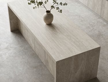 A top-down view of a minimalist kitchen island in light gray stone with a single branch in a vase. Natural daylight.