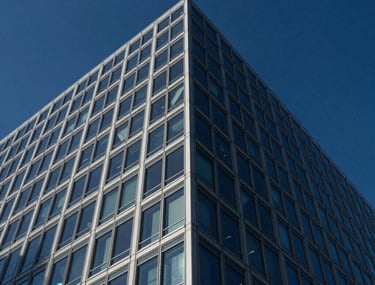 Low-angle shot looking up at the corner of a contemporary corporate headquarters building. The glass facade reflects a deep navy blue sky, emphasizing structural elegance and transparency.