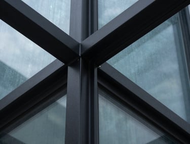 A close-up, sharp architectural detail photograph of matte black metal and glass, with a hint of ice blue light reflecting off a polished surface. The composition is asymmetrical, suggesting precision and high-end engineering.