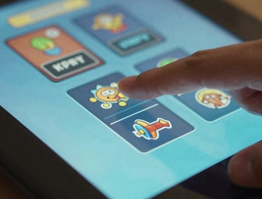 Macro photography of a person's thumb interacting with a colorful touchscreen game menu, light blue and teal glow.