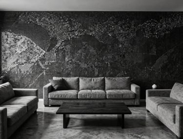 A high-angle architectural photograph of a minimalist Spanish living room with a feature mosaic wall in monochrome black and silver, soft grey furniture, and polished concrete floors.