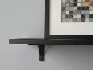 Detail shot of a minimalist black steel shelf against a light grey wall, with a single piece of framed mosaic art, soft shadows, professional photography.