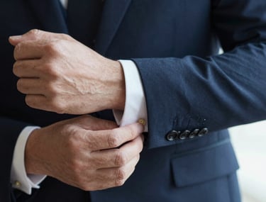 Close-up of a person in a dark suit adjusting their cufflinks. Only hands and suit visible. Cinematic lighting, conveys preparation and meticulous attention to detail.