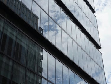 Abstract shot of modern glass architecture reflecting the sky. Sharp angles and high contrast, representing clarity and the structural nature of legal work in a contemporary Brazil.