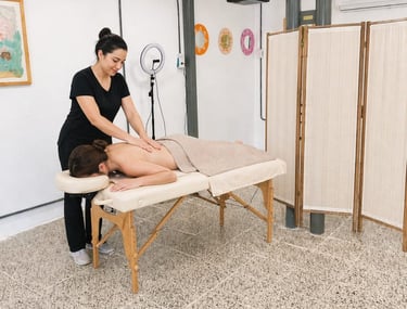 A professional massage therapist performing a back massage on a client in a bright, modern wellness studio.