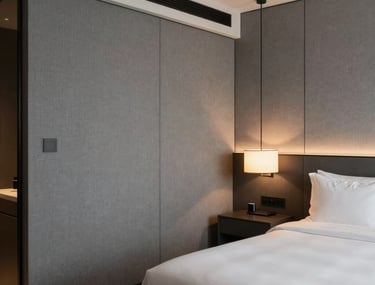 Interior of a modern boutique hotel room in North America with sophisticated gray paneling, luxury fabrics, and warm, minimalist bedside lighting.