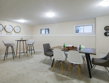 Modern finished basement featuring a wooden dining table with Eames-style chairs and a high-top bistro set.