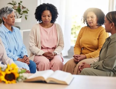Mulheres participando de encontro projeto Maria's reunidas em oração com Bíblia aberta à frente.