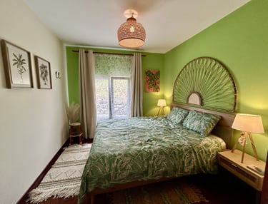 Tropical bohemian bedroom with green walls, rattan headboard, and palm leaf bedding.