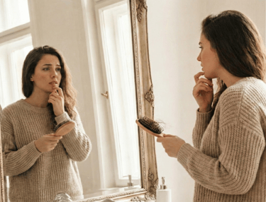 Woman noticing PCOS hair loss in her hairbrush while dealing with hormonal hirsutism on her chin