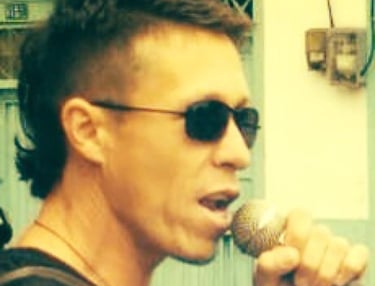 Un vocalista masculino con un corte de cabello mullet moderno y gafas de sol, cantando en un micrófo