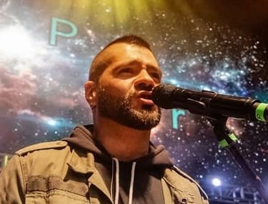 Un cantante masculino con barba interpretando en vivo en el escenario con un micrófono 
