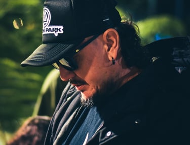 Un hombre con una gorra negra tipo trucker de Linkin Park y gafas de sol, mirando hacia abajo 