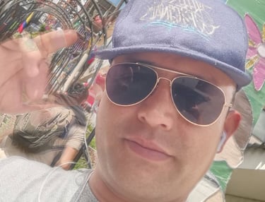 Un hombre con una gorra azul de béisbol y gafas de sol tipo aviador, posando para una selfie al aire