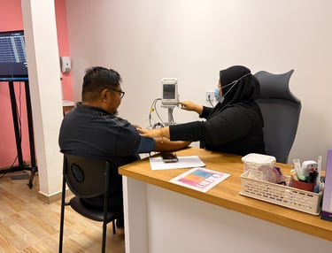 A nurse in a hijab takes a male patient's blood pressure using a digital monitor in a clinic.