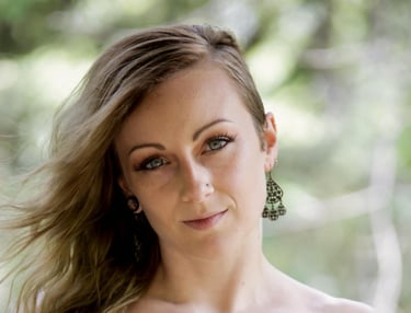 Portrait of a blonde woman with blue eyes wearing ornate bronze chandelier earrings.