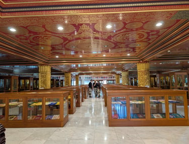 Ornate Buddhist temple interior with red and gold ceilings, showcasing religious texts in glass display cases, and a few