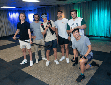 Group of young men, one man wearing a VR headset, one man holding an ice hockey stick