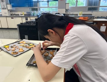 學生雙手擺放甜品於托盤上，動作認真細緻，畫面捕捉學習中的靜心與專注力量。
