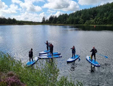 A group of paddle boarders on a calm lake surround by pine forest.