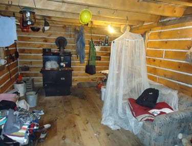 the inside of a log cabin with a wood stove, bed and various supplies