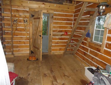 the inside of the log cabin with a ladder leading up to an unseen loft