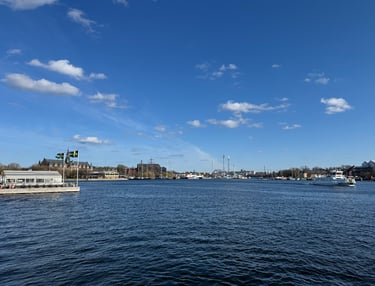 Panoramic view of Stockholm harbor with boats and the Gröna Lund amusement park under a blue sky.