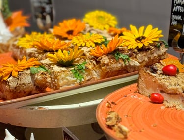 Gourmet apple cake slices decorated with fresh orange flowers and meringue on a dessert display.