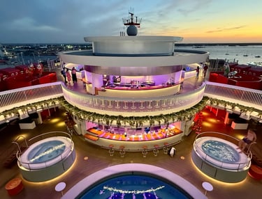 Luxury cruise ship pool deck with illuminated circular bars and hot tubs at sunset.
