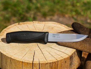 Morakniv Companion bushcraft knife on tree stump with glove in outdoor setting