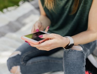 Photo of an adolescent girl with ripped jeans using a smartphone