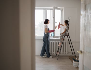 a woman in overalls and a white shirt is painting a window
