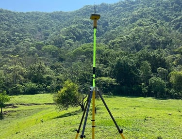 Professional GPS surveying equipment on a tripod in a grassy field with lush green mountains.