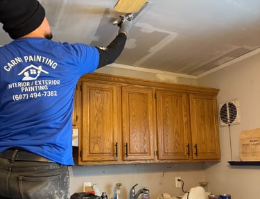 A professional painter from Carni Painting repairs and patches a kitchen ceiling above wood cabinets.